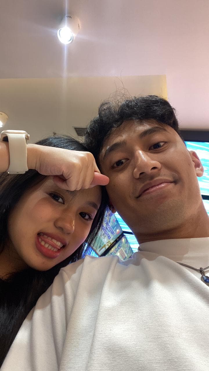 Nayla dan pasangannya berfoto dekat dengan latar layar arcade berwarna biru.