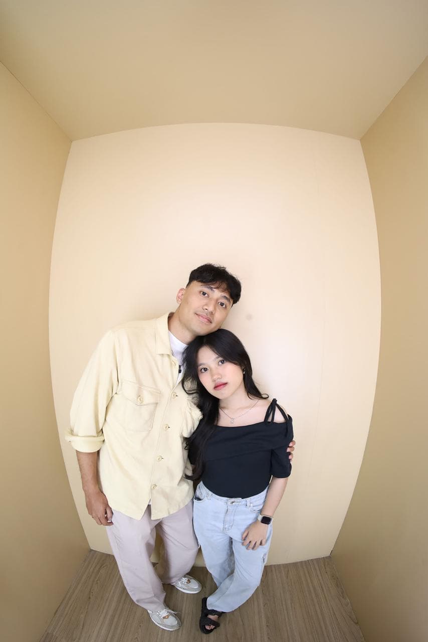 Nayla dan pasangannya tersenyum lembut sambil berdiri berdekatan di ruang krem.