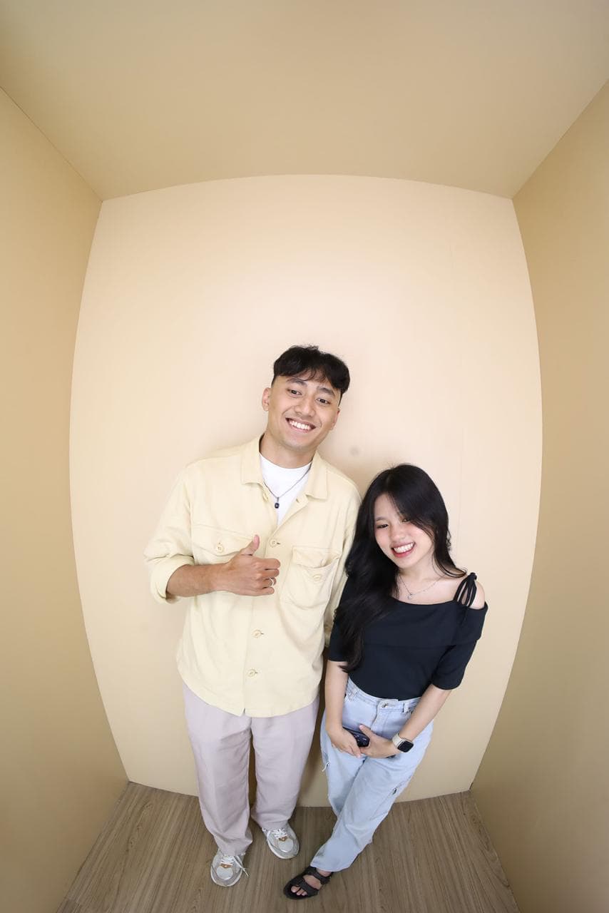 Pasangan tertawa bersama saat sesi foto di ruang krem.