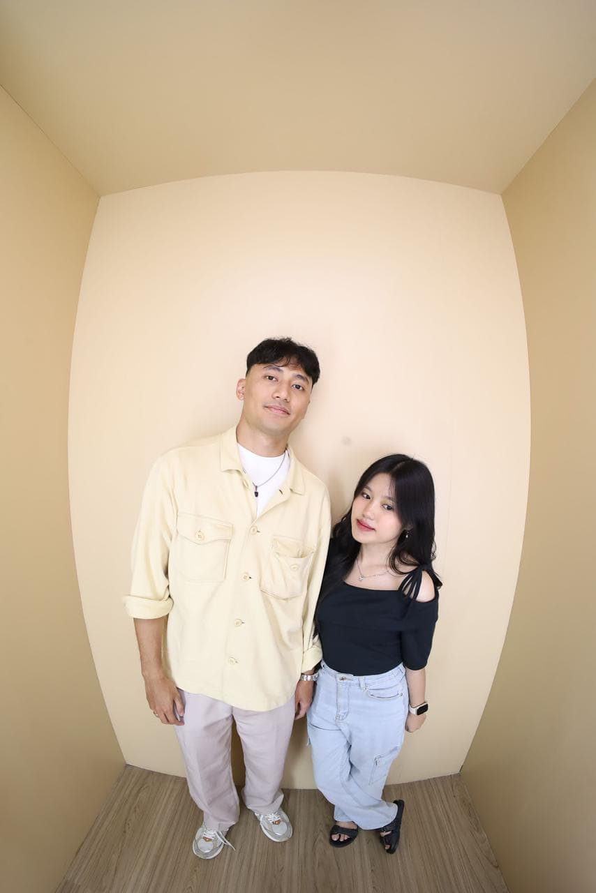 Nayla dan pasangannya berdiri berdampingan sambil tersenyum di ruang krem.