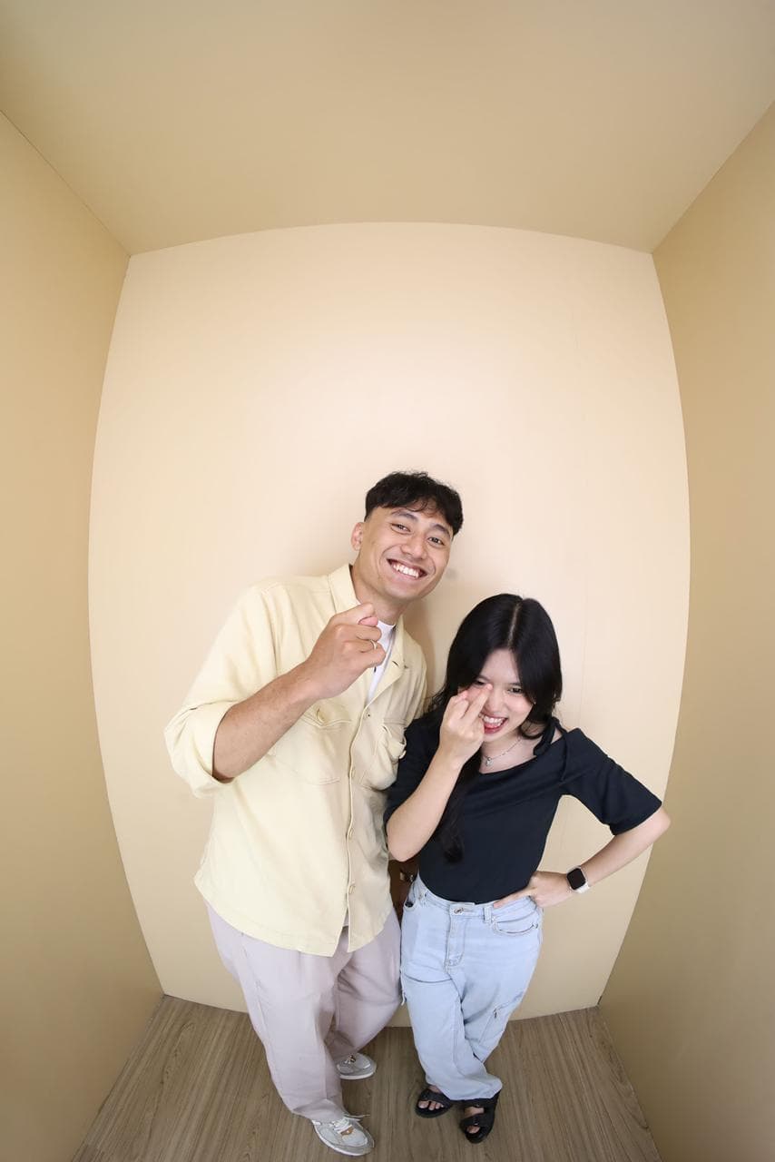 Pasangan tertawa dengan gestur playful di ruang krem.